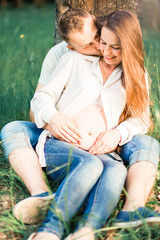 pregnant woman and her husband are sitting on the grass