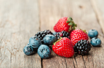 Fresh Summer Berries mix with Strawberry, Raspberry, Red currant, Blueberry and Blackberry on wood background.