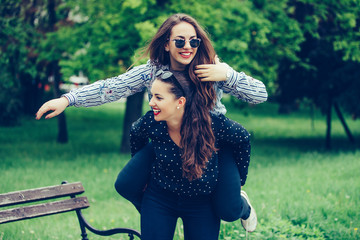 Outdoor shot of young woman carrying her female friend on her back