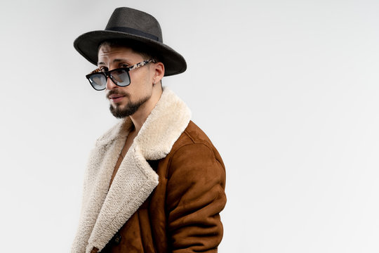 Portrait of young bearded man in black hat and brown coat in black sunglasses isolated over white background, copyspace for your text