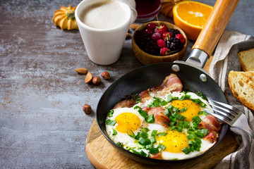 Breakfast scrambled eggs with bacon, coffee, berries, cookies, nuts and juice on dark table surface. Free space for your text.