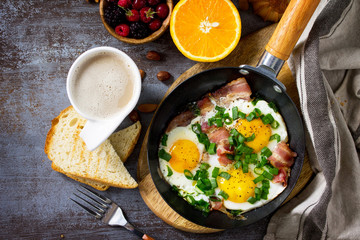 Breakfast scrambled eggs with bacon, coffee, berries, cookies, nuts and juice on dark table surface. Top view flat lay. Free space for your text.