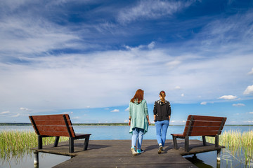 Two young girls girlfriends walk in the fresh air on the pier of the reservoir in beautiful weather on a Sunny spring day. People in solitude with nature. Walking in the fresh air as way of lifestyle.