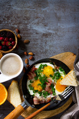 Breakfast scrambled eggs with bacon, coffee, berries, cookies, nuts and juice on dark table surface. Top view flat lay. Free space for your text.