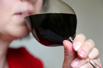 Glass of red wine in female hand, white woman in red dress drinking alcohol. Concept of...