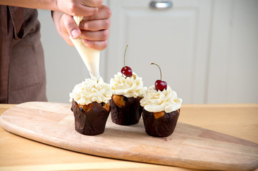 Female baker decorating cupcake with cherry and creme
