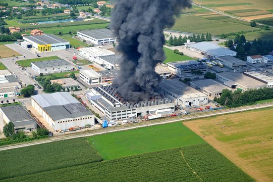 Factory fire with black smoke that causes pollution exits the building and firefighters at work