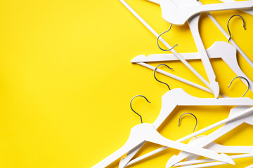 White clothes hangers on yellow background with copy space. Flat lay. Top view. Minimalism style....