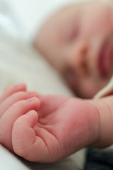 Hands of sleeping newborn baby. Face in shallow depth of field.