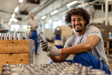 Happy African American worker checking quality of manufactured steel parts.