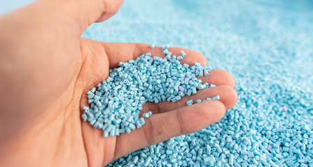 Hand on large pile of blue plastic granules in temporary storage of production line at recycle...