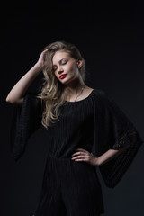 Beautiful ,young blonde with bright red lips and expressive eyes in a black jumpsuit. Beauty portrait of a girl. Emotional and bright appearance. Fashion portrait of a woman.