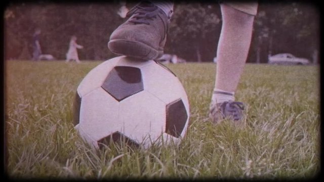 Boy puts his foot on a soccer ball. Brown shoes. Family video. Archived video. Old film. Famous footballer in childhood. Worn sneakers, boots. Ball on green grass.  Family holiday. Training. Health.
