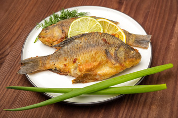 Fried carp fish on white plate. Ready meal. Wooden background