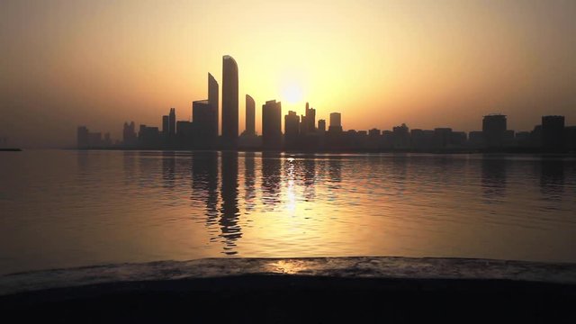 Woman in a long skirt walking across the camera at sunrise. Cityscape of Abu Dhabi at the background.