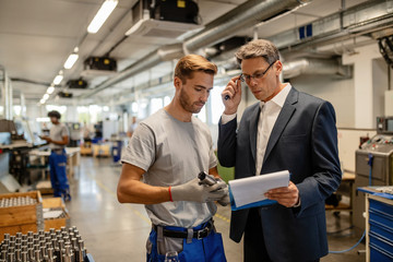 Quality control inspector and metal worker reading reports in industrial building.