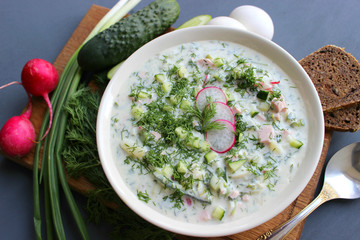 Okroshka is a traditional Russian summer cold soup in a ceramic bowl. Ingredients potatoes, radishes, cucumbers, dill, eggs, kefir (yogurt), sausage. Summer yogurt cold soup on a wooden table. Selecti