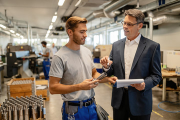 Happy engineer and steel worker communicating while going through reports in a factory,