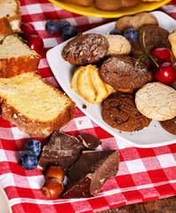 Oatmeal Cookies and sand chocolate cake with blueberries on wooden table with gingham cloth in farm style close up. Table setting breakfast for two with cups in. How and from what make sweets.