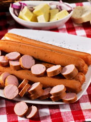 Sausage portion with bread baguette on table setting on checkered tablecloth and cup in farm style. High carbohydrate content.