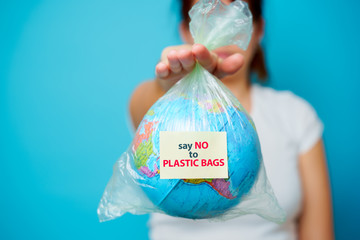 Woman holds in hands plastic bag with sticker text say NO to PLASTIC BAGS and planet earth at blue...