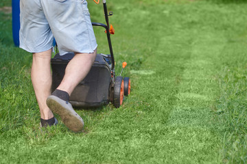 European man is working on the personal plot, he is using lawn mower. © Artem