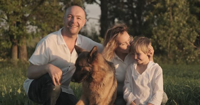 Happy family with a dog in nature. 7 year old boy with his parents petting a dog breed German shepherd. Father, mother and son  are on the field with dog. Happiness concept. Slow motion