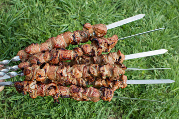 Cooked shashlik on skewers  against green grass background.  Meat kebab  in the open air.