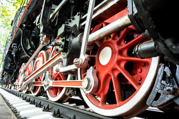 Red wheels with a white rim on a black train background. Old steam locomotive parked in a museum. Spring. Day.