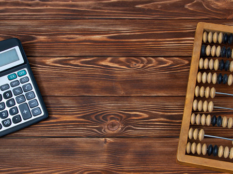 On a brown wooden table with a texture are old abacus and a calculator. Free space for an inscription or a title.