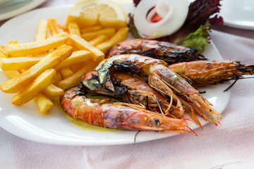 Close up big size grill shrimps with fried potato, vegetables and lemon, lunch time in restaurant.
