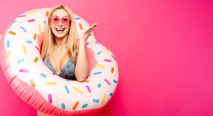 Obraz na płótnie Canvas Photo of girl in swimsuit sunglasses with inflatable donut for swimming on empty pink background. Indicates with hand to side
