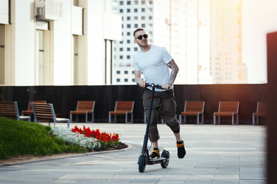 Attractive man riding electric kick scooter at cityscape background.