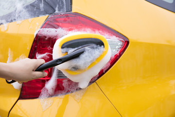 Close-up Of Hand With sponge Washing yellow Car