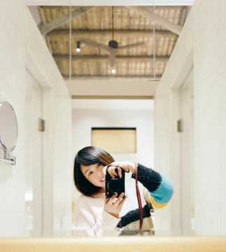 portrait of woman holding camera in front of a mirror in room