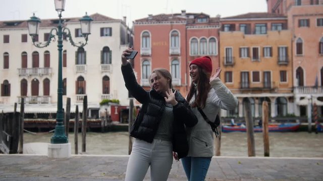 Two young smiling women standing on a background of a channel and take selfie