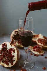 Red wine with an open pomegranate on a textured gray concrete background. A man pours red wine from a bottle into a glass.