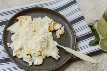 Delicious cooked omelet on a gray napkin and beige carpet. Homemade lemonade and scrambled eggs for breakfast. Dark dishes on a light background.