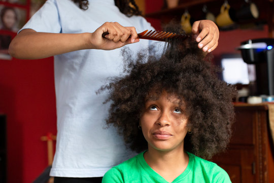 Portrait of a pretty teenage girl sitting as her sister helps her comb her kinky curly hair