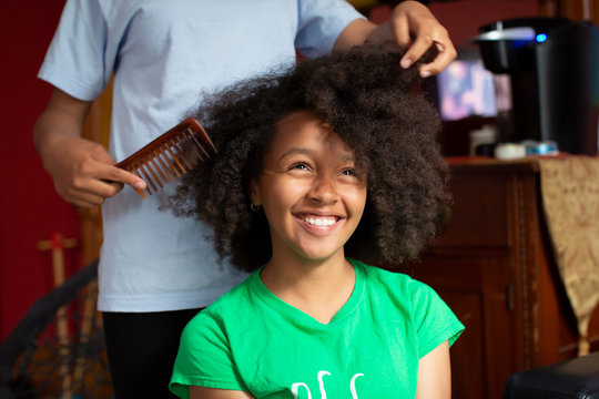 Portrait of a pretty teenage girl sitting as her sister helps her comb her kinky curly hair