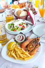 Plate with fresh greek salads, shrimp, potato fried, beers and bread, olive oil on a table. Traditional Greek dish.