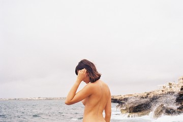 Shirtless woman standing on seashore