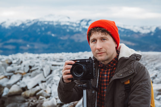 Portrait traveler photographer man taking nature video of mountain landscape. Professional videographer on adventure vacation shooting camera on tripod. 