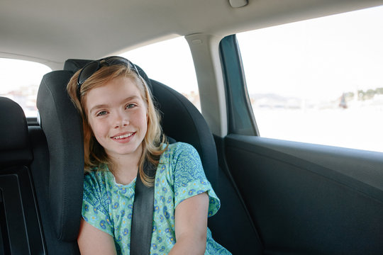 Lovely blonde girl in turquoise dress sitting in child seat in the car