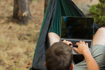 Man working on laptop in hammock in forest