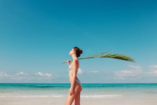 Fototapeta Woman holding a palm leaf on the beach