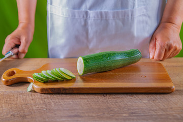 Guy cutting a zukini in slices. A knife and green zukini