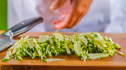 Chef cutting green zucchini into thin slices on wooden board in kitchen, Close-Up