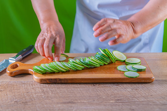 Guy cutting a zukini in slices. A knife and green zukini