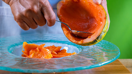 Closeup of hands holding a papaya. cutting little pieces with spoon